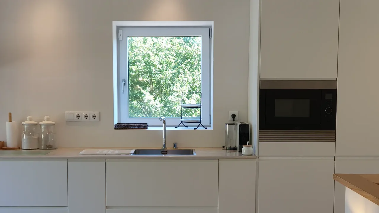 Bright modern kitchen with white cabinetry and a window overlooking trees.